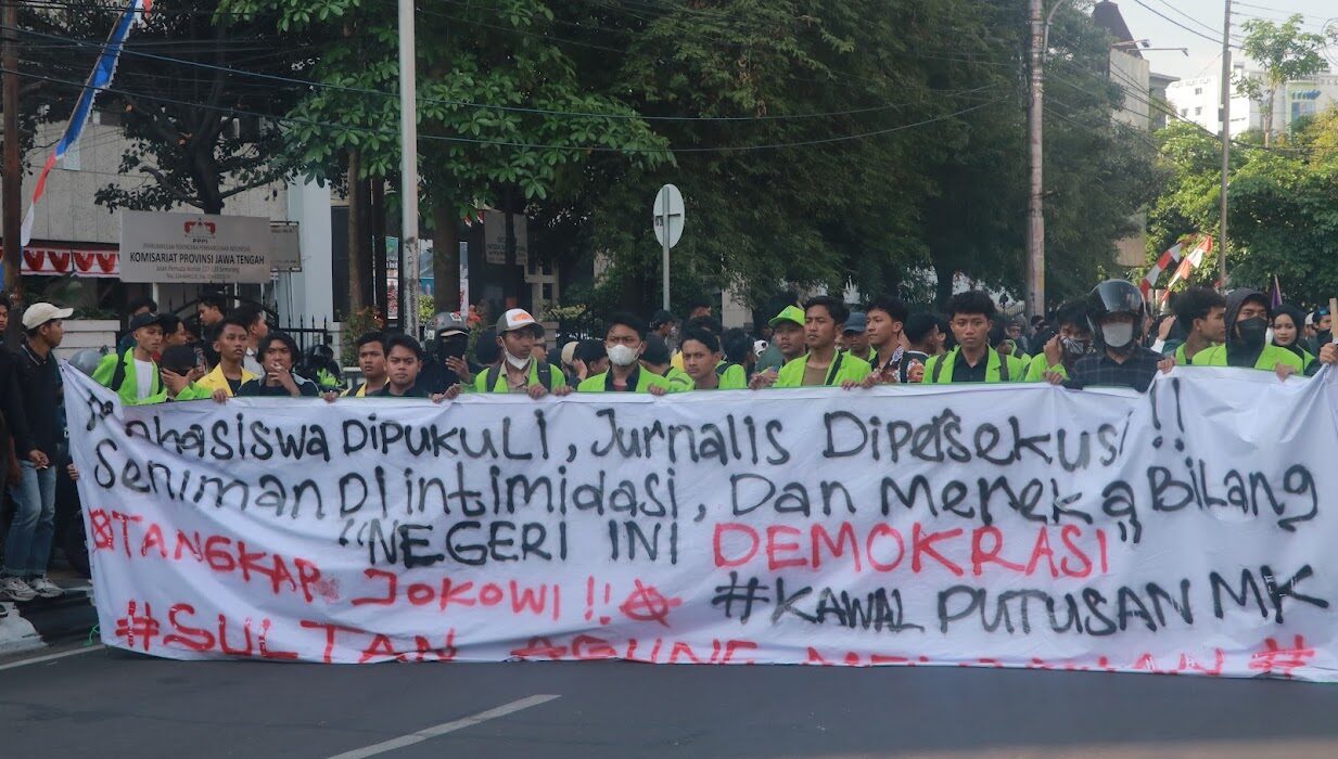 Spanduk sindiran terhadap penyelewengan demokrasi dan represifitas polisi dibentangkan dalam perjalanan menuju titik aksi, Senin (26/08). [BP2M/Anastasia]