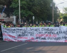 Spanduk sindiran terhadap penyelewengan demokrasi dan represifitas polisi dibentangkan dalam perjalanan menuju titik aksi, Senin (26/08). [BP2M/Anastasia]