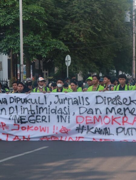 Spanduk sindiran terhadap penyelewengan demokrasi dan represifitas polisi dibentangkan dalam perjalanan menuju titik aksi, Senin (26/08). [BP2M/Anastasia]