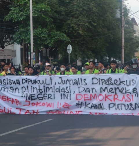 Spanduk sindiran terhadap penyelewengan demokrasi dan represifitas polisi dibentangkan dalam perjalanan menuju titik aksi, Senin (26/08). [BP2M/Anastasia]