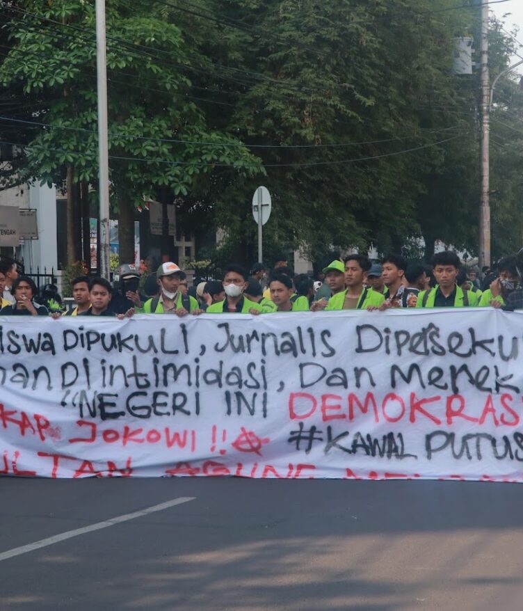 Spanduk sindiran terhadap penyelewengan demokrasi dan represifitas polisi dibentangkan dalam perjalanan menuju titik aksi, Senin (26/08). [BP2M/Anastasia]