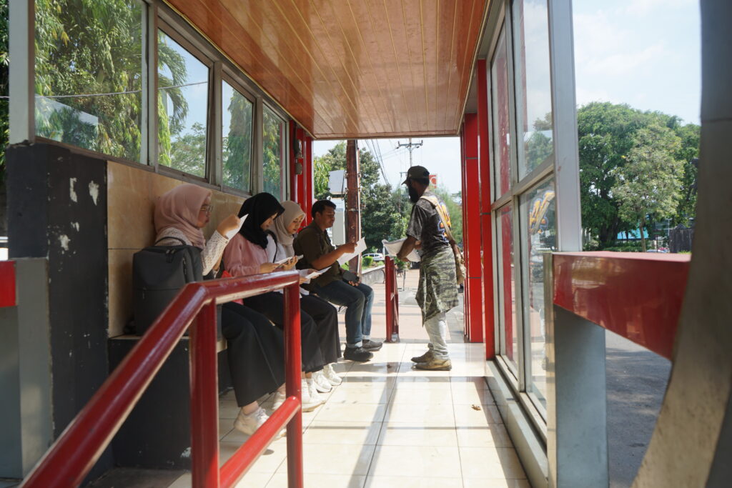 Seorang massa aksi membagikan lembar kajian di halte transportasi publik yang memuat tentang kondisi di Papua terkini. (Rabu, 28/05/2025) [Lidwina/BP2M]
