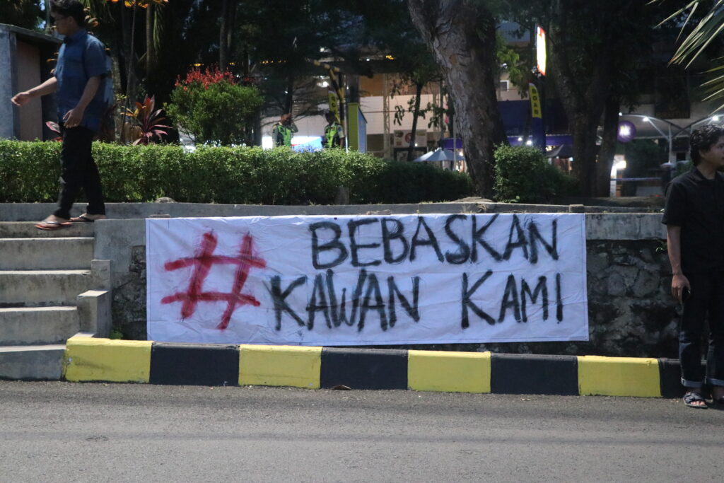 Sebuah spanduk terbentang di Taman Simpang Tujuh bertuliskan “Bebaskan Kawan Kami”. (Kamis, 19/07/2025) [Sultan/Magang BP2M]
